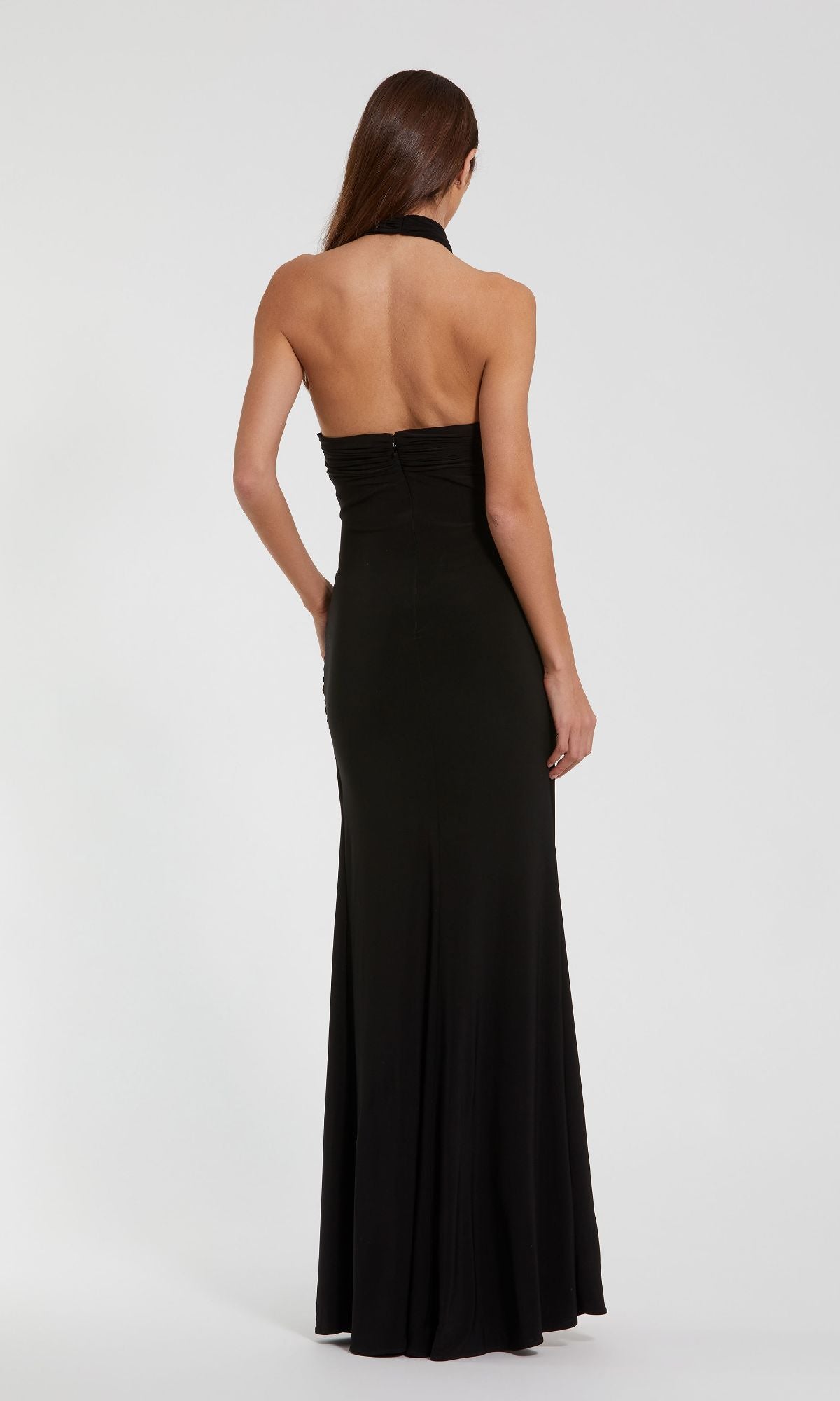 A woman faces away, wearing the Cut-Out Black Halter Prom Dress: Mac Duggal 27572, featuring a fitted bodice and floor-length skirt, set against a plain white background.