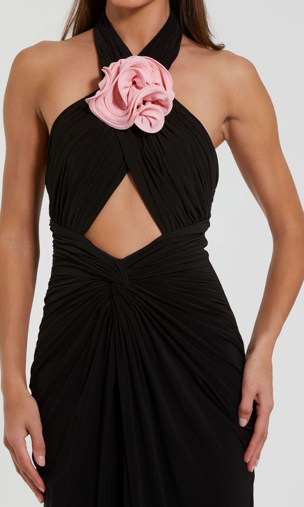 A woman wears the Cut-Out Black Halter Prom Dress, Mac Duggal 27572—a striking black halter gown with a central cutout and a bold pink flower at the neckline, ideal for formal evening events.