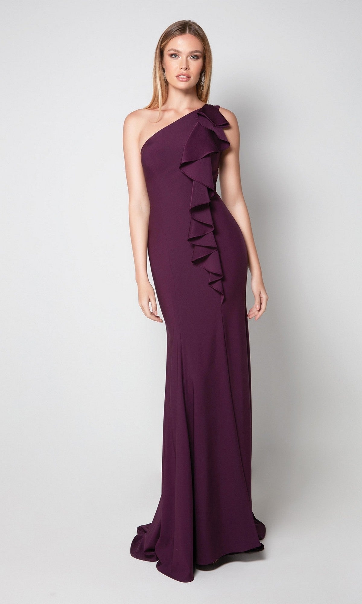 Woman wearing the Alyce 27575 long formal dress in deep amethyst, featuring a one shoulder design with ruffle detailing down the front, standing against a plain light background.