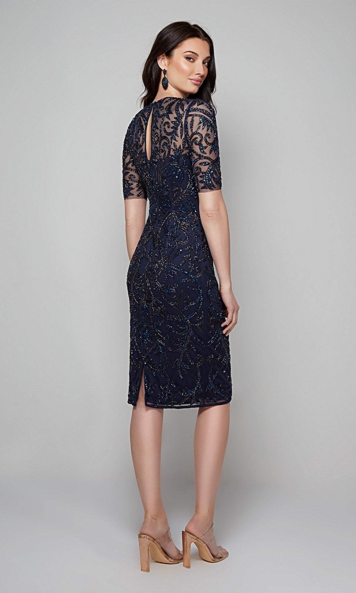 A woman in the Alyce 27583 knee-length semi-formal dress, featuring navy blue sheer sleeves and beaded detailing, stands in heels with her back to the camera.