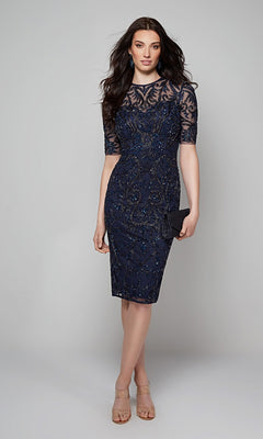 A woman in the Alyce 27583 knee-length semi-formal dress, featuring navy blue lace and intricate beadwork, poses with a chic clutch against a plain grey background.