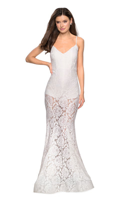 A woman wearing the Sheer Lace Mermaid Prom Dress: La Femme 27584, a sleeveless white lace gown with thin straps and delicate lace details on the skirt, stands against a plain white background.