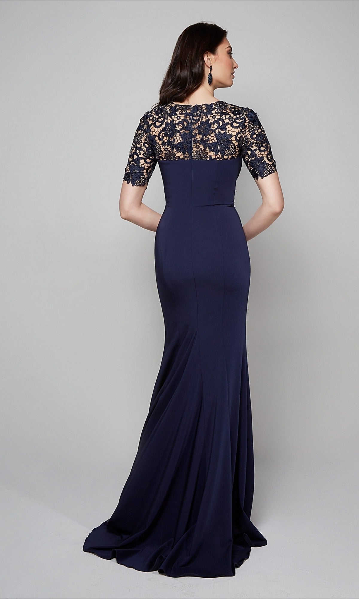 A woman stands with her back to the camera wearing the Alyce 27585, a floor-length navy formal dress featuring a fitted lace bodice and short sleeves.