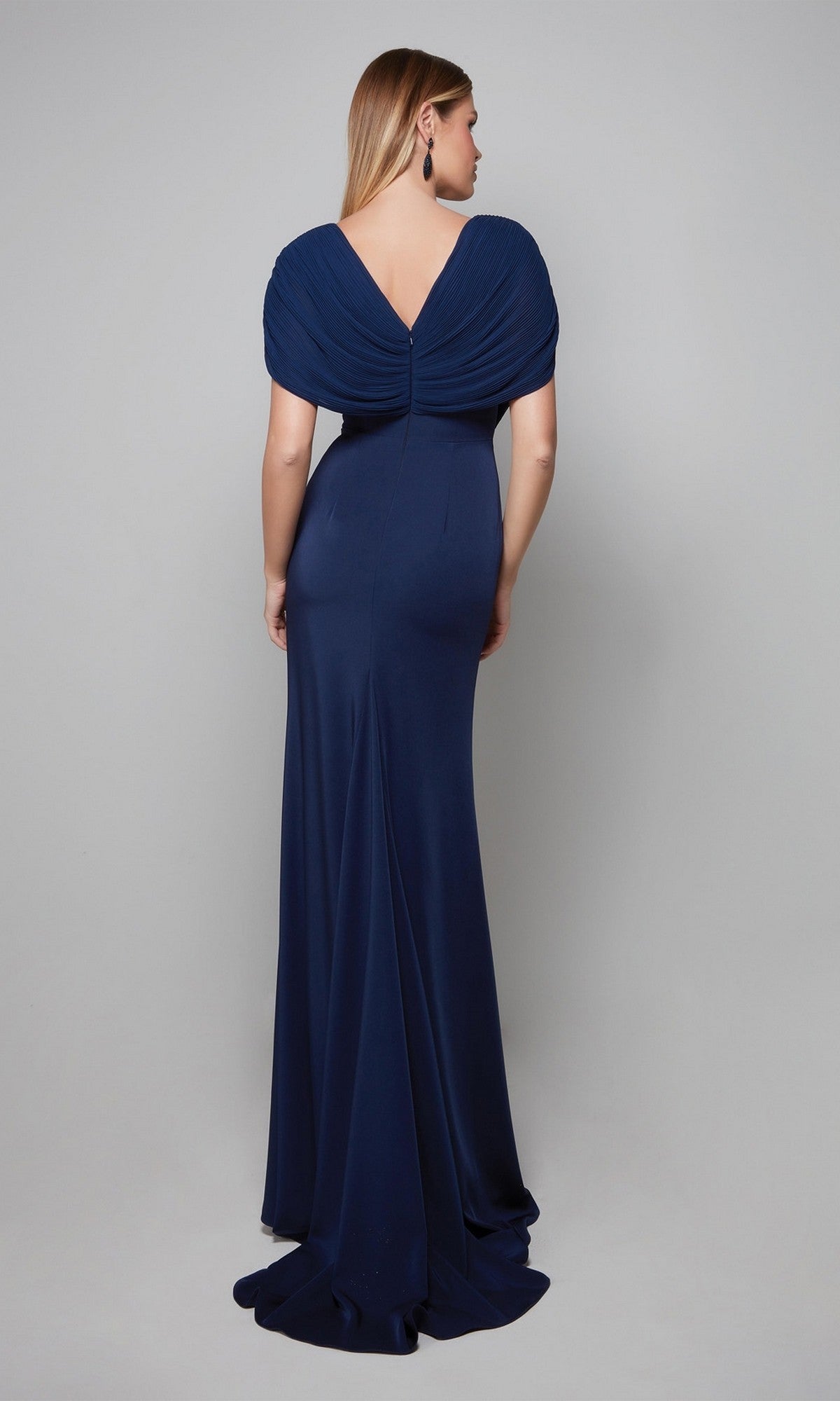 A woman faces away, modeling the Alyce 27591 long formal dress in navy blue crepe with a V-back and cap sleeves, set against a plain light gray background.