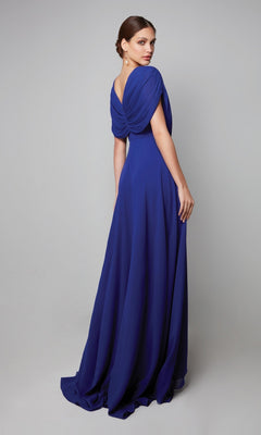 Woman wearing the Alyce 27592 long formal dress in royal blue, featuring chiffon fabric, elegant cape sleeves, and draped back detailing, standing against a plain gray background.