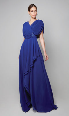 A woman models the Alyce 27592, a royal blue floor-length chiffon dress with draped layers and cape sleeves, against a plain light gray background.