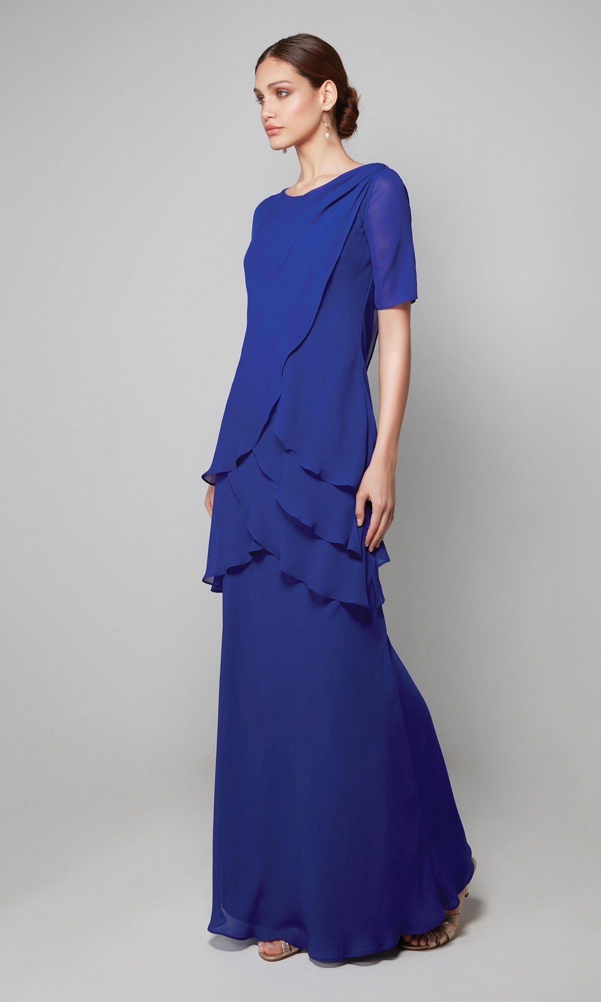 A woman stands against a light gray background wearing the Alyce 27593 long formal dress—a floor-length royal blue chiffon gown with tiered layers and short sleeves. Perfect for a sophisticated mother-of-the-bride look.