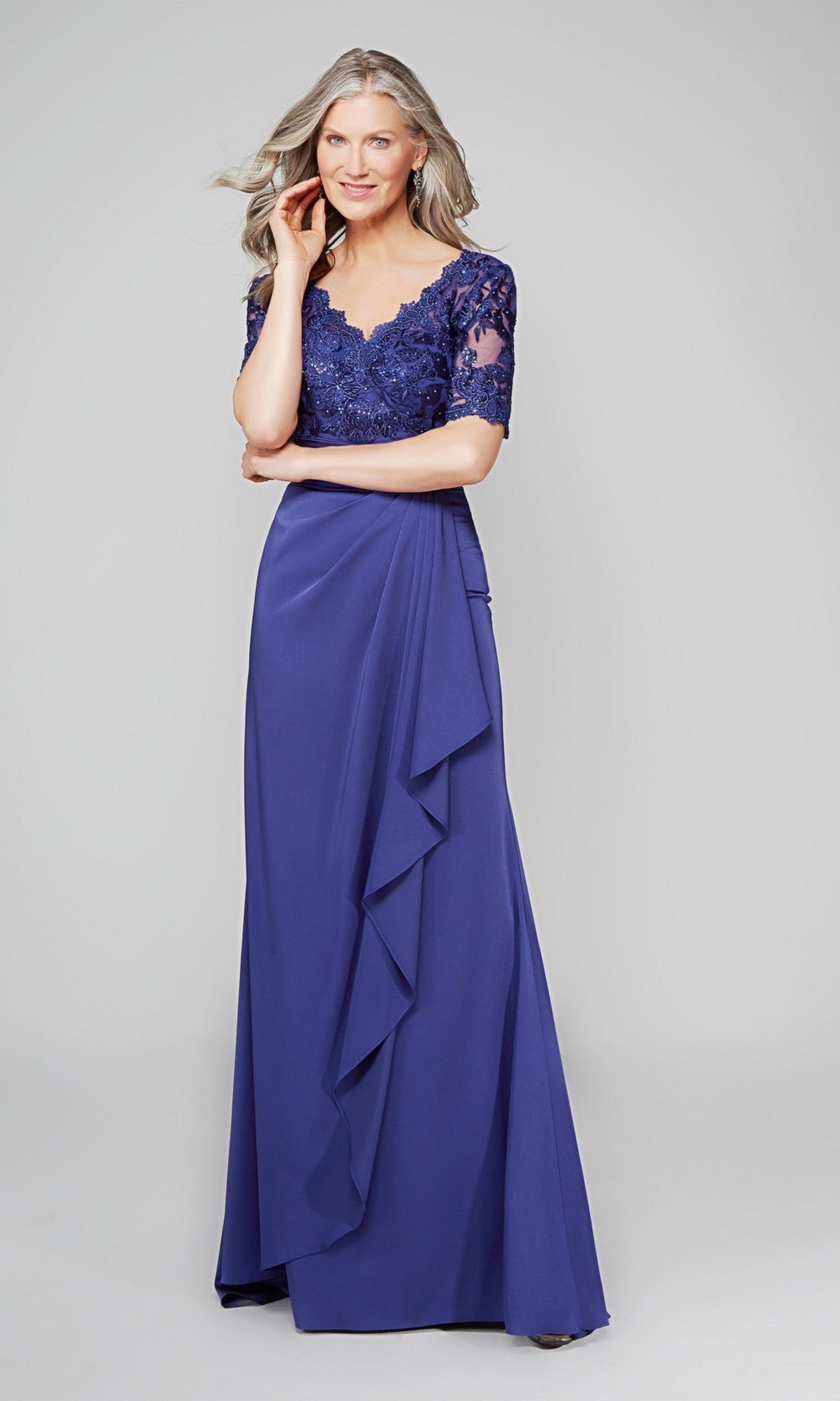 A woman wears the Alyce 27595, a long formal purple mother-of-the-bride dress with short sleeves, a lace bodice, and an elegant sheath skirt, standing against a plain light background.
