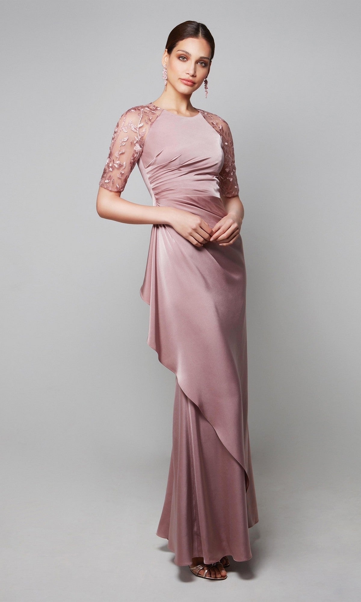 A woman wears the Alyce 27601 long formal dress in mauve, featuring draped fabric and short sheer floral-embroidered sleeves; perfect as a mother-of-the-bride gown, shown against a neutral background.