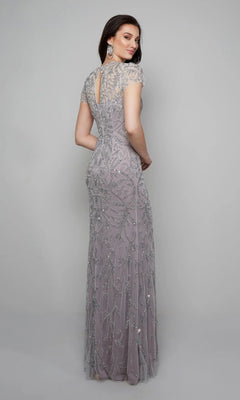 A woman faces away, wearing the Alyce 27607 long formal dress in lilac. This floor-length gown features short sleeves, a keyhole back, and intricate beaded embellishments, all set against a plain gray background.