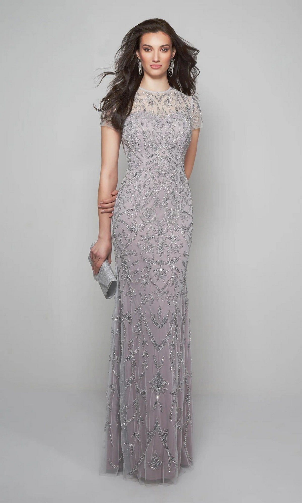 A woman in the Alyce 27607 long formal dress—a floor-length, beaded lavender evening gown with short sleeves—holds a silver clutch while standing against a plain light gray background.