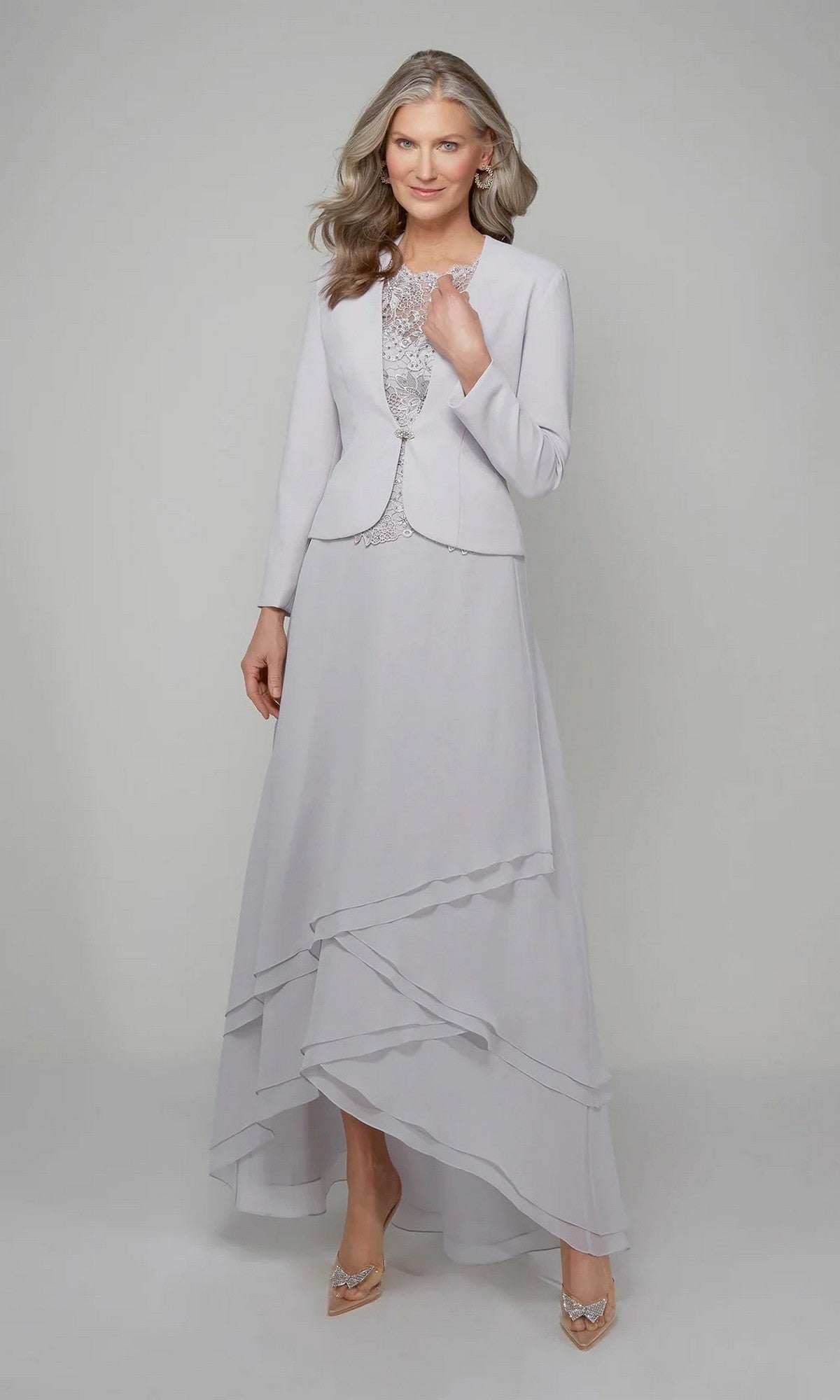 A woman with long gray hair wears the Alyce 27608 long formal dress in Sterling, featuring a beaded lace bodice, matching jacket, and layered skirt, standing against a plain light background.