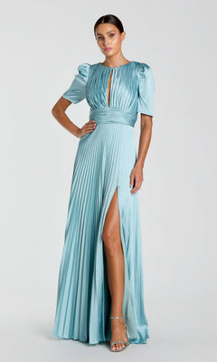 A woman wears the Mac Duggal 27616 Long Formal Dress in French Blue, featuring pleats, a floor-length cut, short puff sleeves, front keyhole, high waist, and a thigh-high slit—styled with strappy heels.