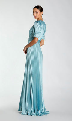 A woman poses sideways in the Mac Duggal 27616 long formal dress, featuring light blue pleats and short puff sleeves, exuding timeless elegance against a plain background.