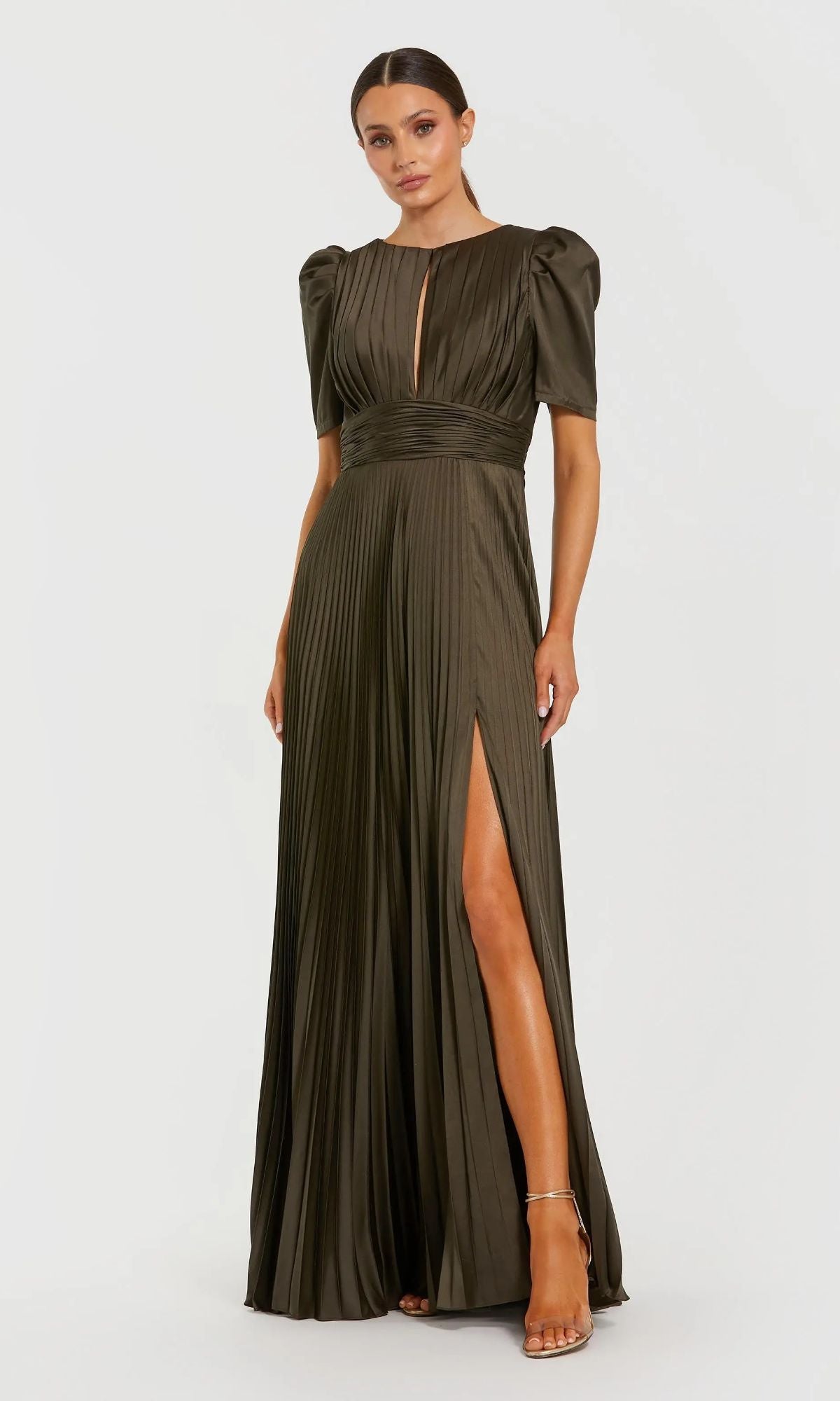 A woman wears the Mac Duggal 27616 long formal olive dress with pleats, short puff sleeves, waistband, front keyhole, and high slit, standing against a plain light background.