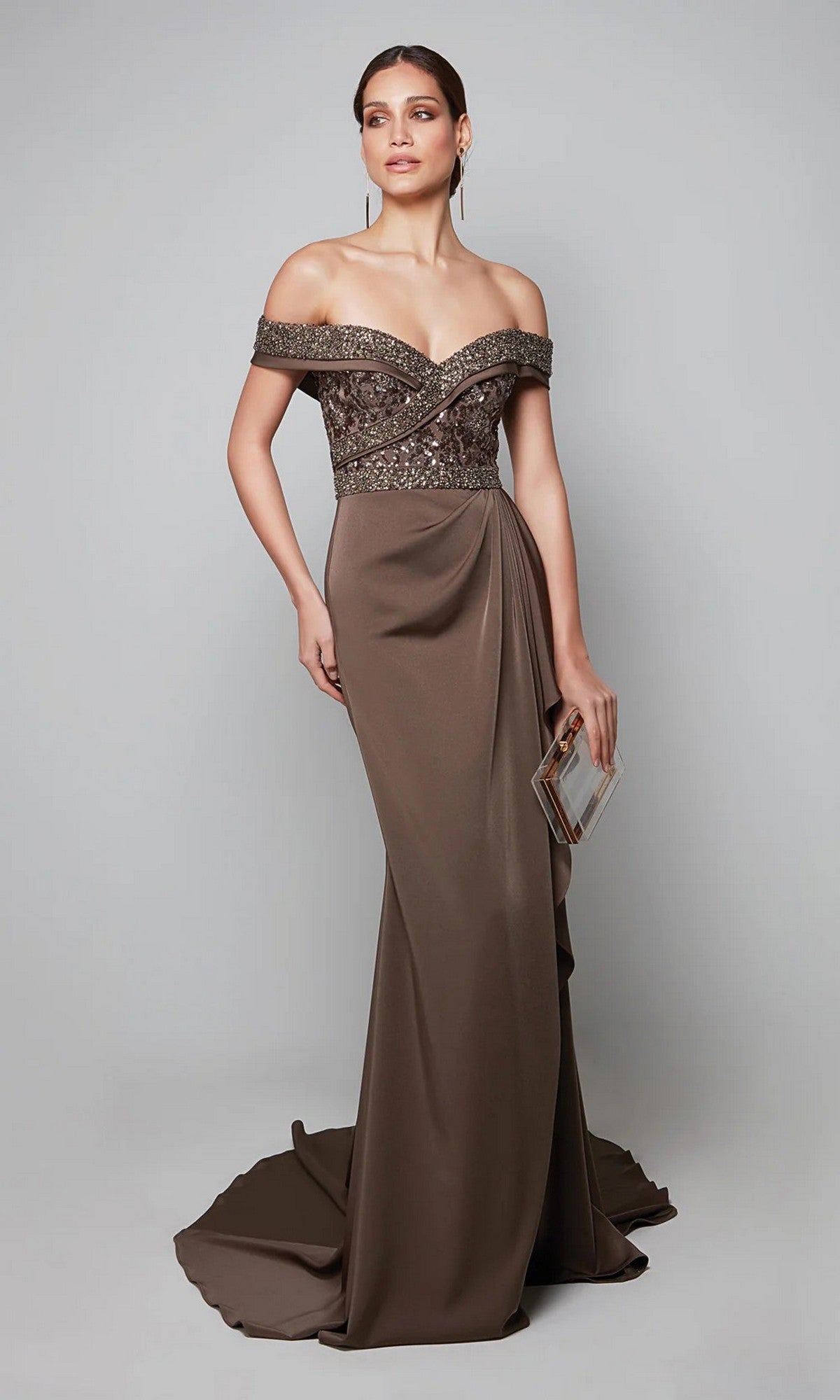 Woman in the Alyce 27619 long formal dress featuring an off-the-shoulder, brown beaded bodice and floor-length skirt, holding a small box clutch against a plain background.