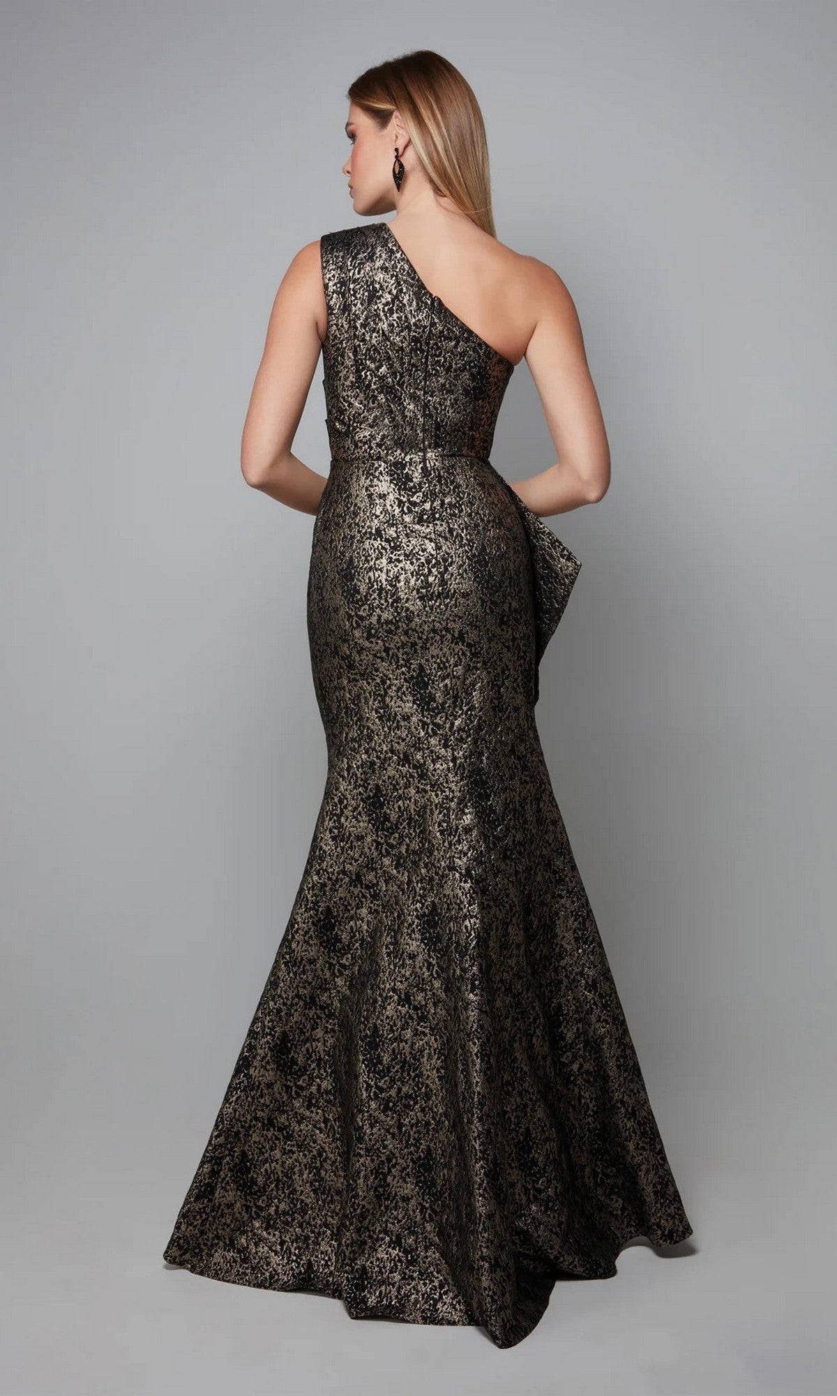 A woman models the Long Formal Dress: Alyce 27620—a metallic, one-shoulder gown with a fitted waist—standing against a plain gray background, facing away from the camera.