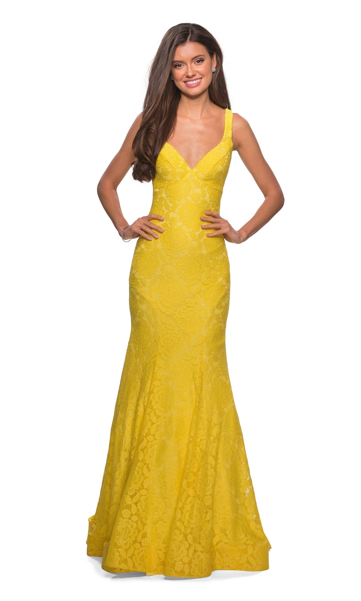 A woman stands smiling, wearing La Femme 27623, an open-back, floor-length yellow lace mermaid prom dress with a sleeveless V-neckline.
