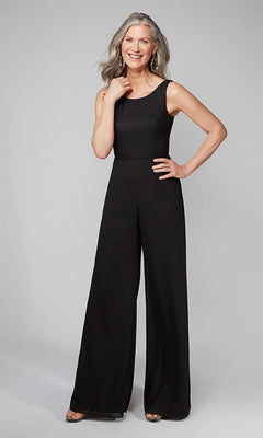 A woman with gray hair smiles against a plain light gray background, wearing the Long Formal Jumpsuit: Alyce 27633 with sheer ruffled sleeves and sandals.