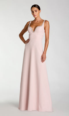 A woman wearing the Mac Duggal 27633 long formal dress in dusty rose, featuring a pale pink crepe fabric with a deep V-neckline and sparkling rhinestone trim, stands against a plain light gray background. This elegant design showcases the signature evening wear style of Mac Duggal.