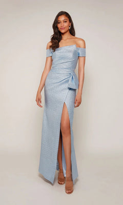 A woman wears the Alyce 27639 long formal dress—a light blue, off-the-shoulder gown with a side slit and bow detail—paired with nude heels, posing against a plain background.