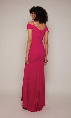A woman stands in a studio, back to camera, wearing the Alyce 27645 long formal dress—a bright pink, floor-length gown featuring an off-the-shoulder neckline, fitted bodice with beaded embroidery, and a flowing skirt.