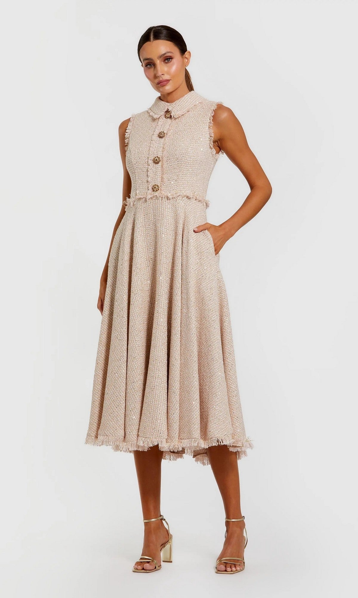 A woman models the Mac Duggal 27658 semi-formal midi dress, a sleeveless boucle design with large front buttons, one hand in her pocket and paired with strappy heels.