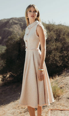 A woman stands outdoors against hills and trees, wearing the blush Mac Duggal 27658 Semi-Formal Midi Dress, styled sleeveless with bracelets and earrings.