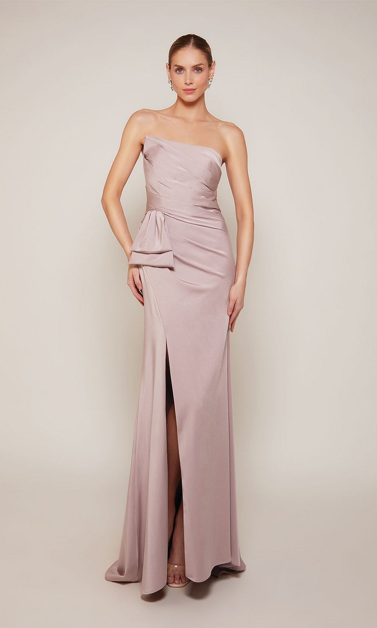 A woman poses against a plain light background in the Alyce 27658 long formal dress—a strapless light mauve stretch crepe gown with a side bow and front slit, perfect for a mother of the bride.