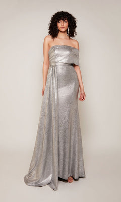 A person stands against a plain light background wearing the Alyce 27663 long formal dress, featuring a silver metallic jacquard fabric, off-the-shoulder neckline, draped detail, and a thigh-high side slit.