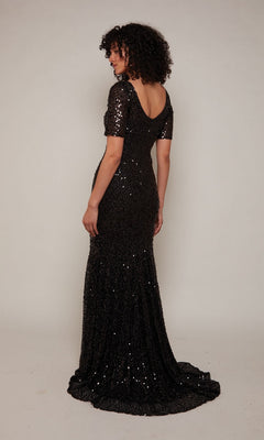 A woman with curly hair models the Alyce 27668 sequin long formal dress, showcasing short sleeves and a low back—an elegant choice for evening occasions against a plain light background.