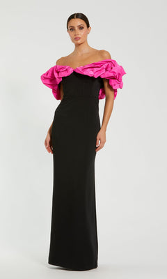 A woman models the Mac Duggal 27669 Hot Pink and Black Prom Gown, an off-the-shoulder evening dress with a fitted black bodice, floor-length skirt, and bold hot pink ruffled neckline against a plain light background.
