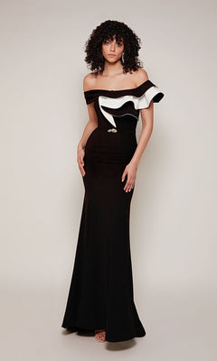 A woman wears the Alyce 27672 long formal dress in black/ivory, featuring a floor-length, off-the-shoulder sheath silhouette with two-tone ruffle detail, standing against a plain light background.