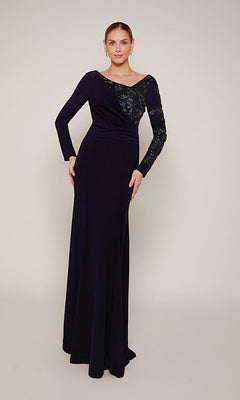 A woman stands wearing the Alyce 27675 long formal dress in navy, featuring sequin detailing on one sleeve and the upper bodice, a beaded V-neckline, and a fitted silhouette for an elegant look.