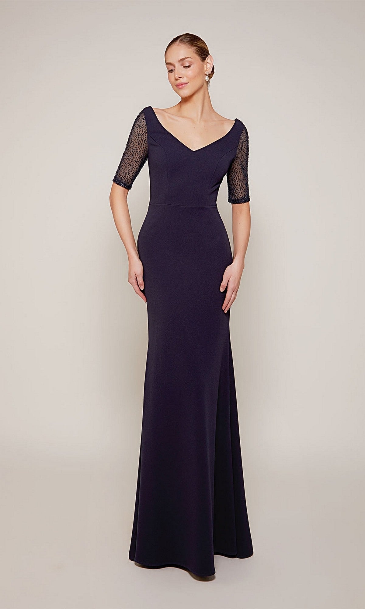 Woman in the navy Alyce 27677 long formal dress with sheer lace half sleeves, perfect for black-tie events or as a striking mother-of-the-bride look, standing against a plain light background.