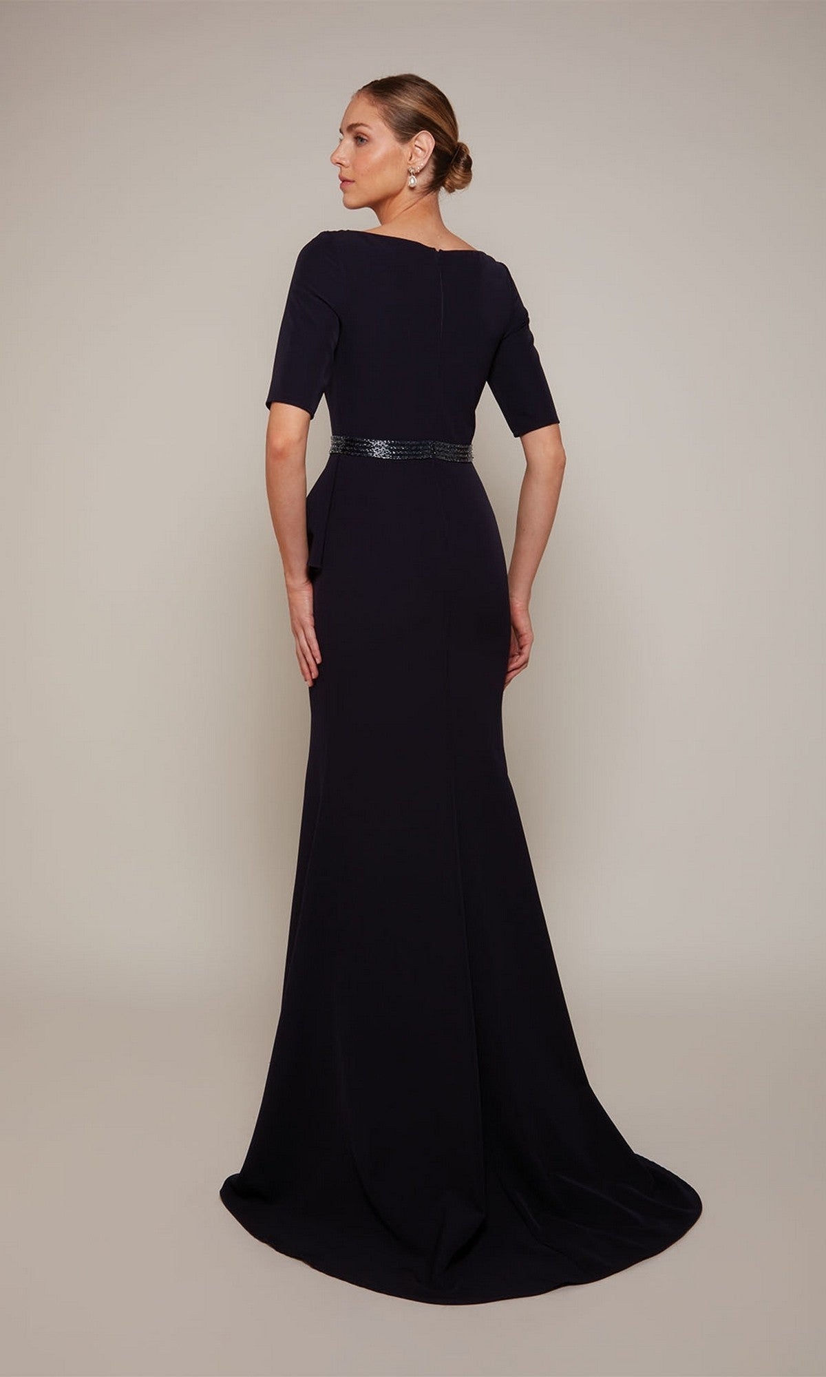 Woman wearing the Alyce 27679 long formal dress—navy, floor-length with a fitted bodice and sequin belt—stands against a plain background, facing away from the camera.