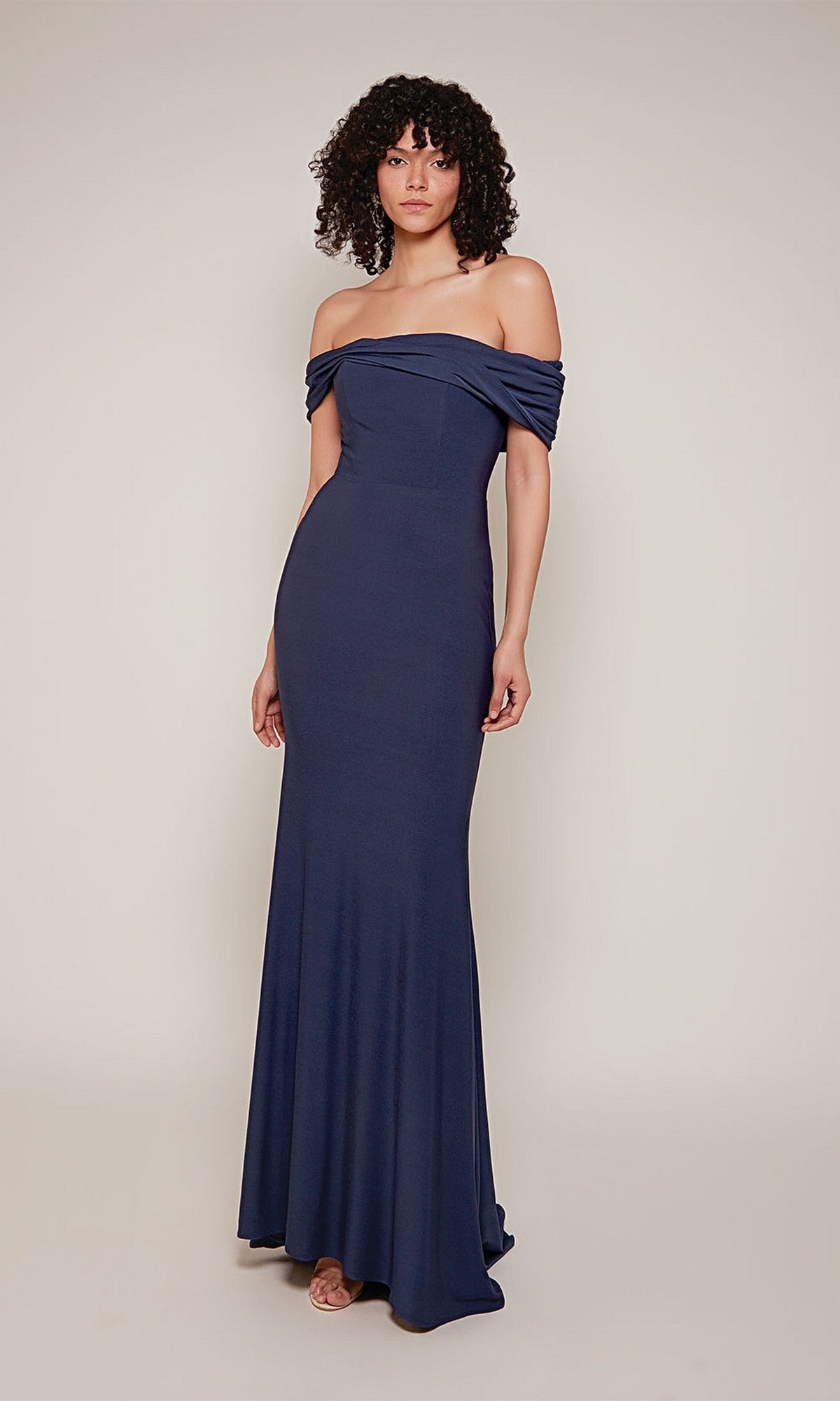 A woman stands against a light background, modeling the Alyce 27680 long formal dress in navy, featuring an off-the-shoulder design with a fitted bodice and flared skirt.