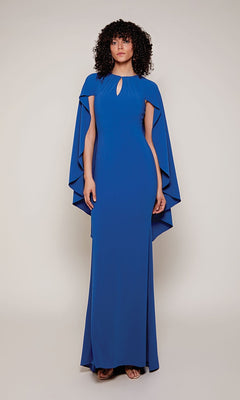 Someone wearing the Alyce 27683 long formal dress—floor-length, fitted, royal blue with high-low cape sleeves—stands against a plain light background.