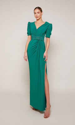 A woman wears the Alyce 27690 long formal dress in emerald, featuring puffed short sleeves, a V-neckline, beaded waist belt, gathered detailing, and a high side slit.