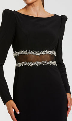 A woman wearing the Mac Duggal 27695 long formal dress—a black stretch jersey gown featuring long sleeves, sheer midsection, puff shoulders, and silver leaf embellishments at the waist for an elegant evening look.