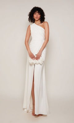 A woman wears the Alyce 27697 long formal dress, a white one-shoulder satin gown with a thigh-high slit, posing with a small white floral accessory—a perfect pick for prom or any formal event.