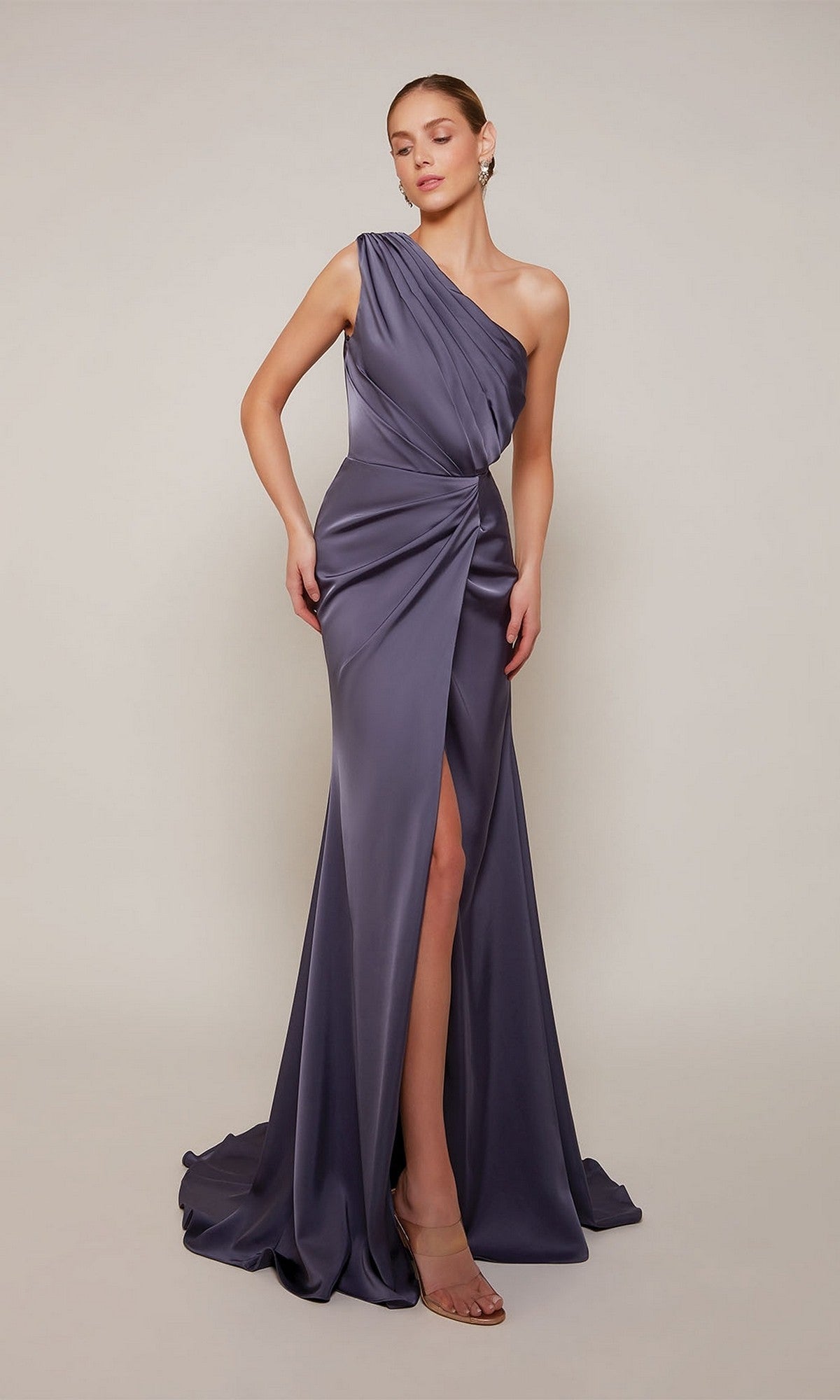 A woman models the Alyce 27697 long formal dress—a floor-length, one-shoulder satin gown in muted purple with a thigh-high slit—against a plain background, highlighting its elegant style ideal for prom.