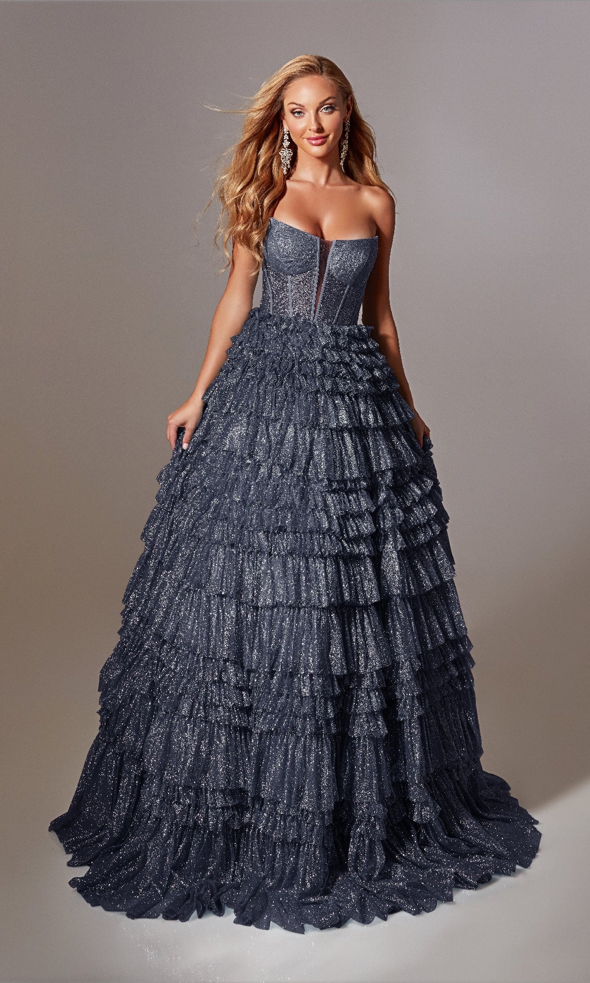 A woman models the Strapless Long Prom Ball Gown: Aerie Couture 276, showcasing its dark blue ruffled full skirt and fitted bodice against a plain background.