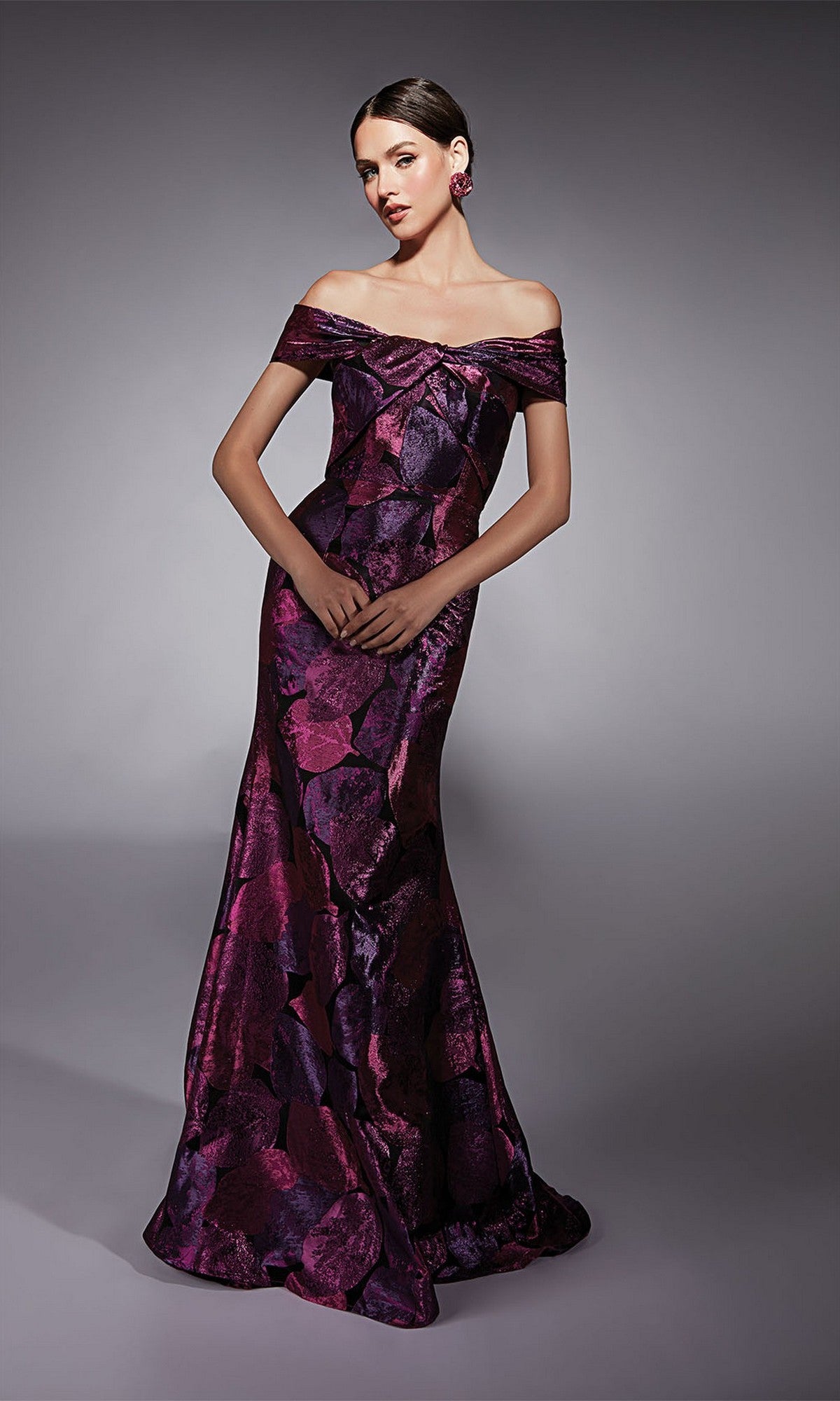 A woman in the Alyce 27702 long formal jacquard off-the-shoulder gown with purple and dark pink floral pattern, ideal for a mother of the bride, stands against a neutral gray background.