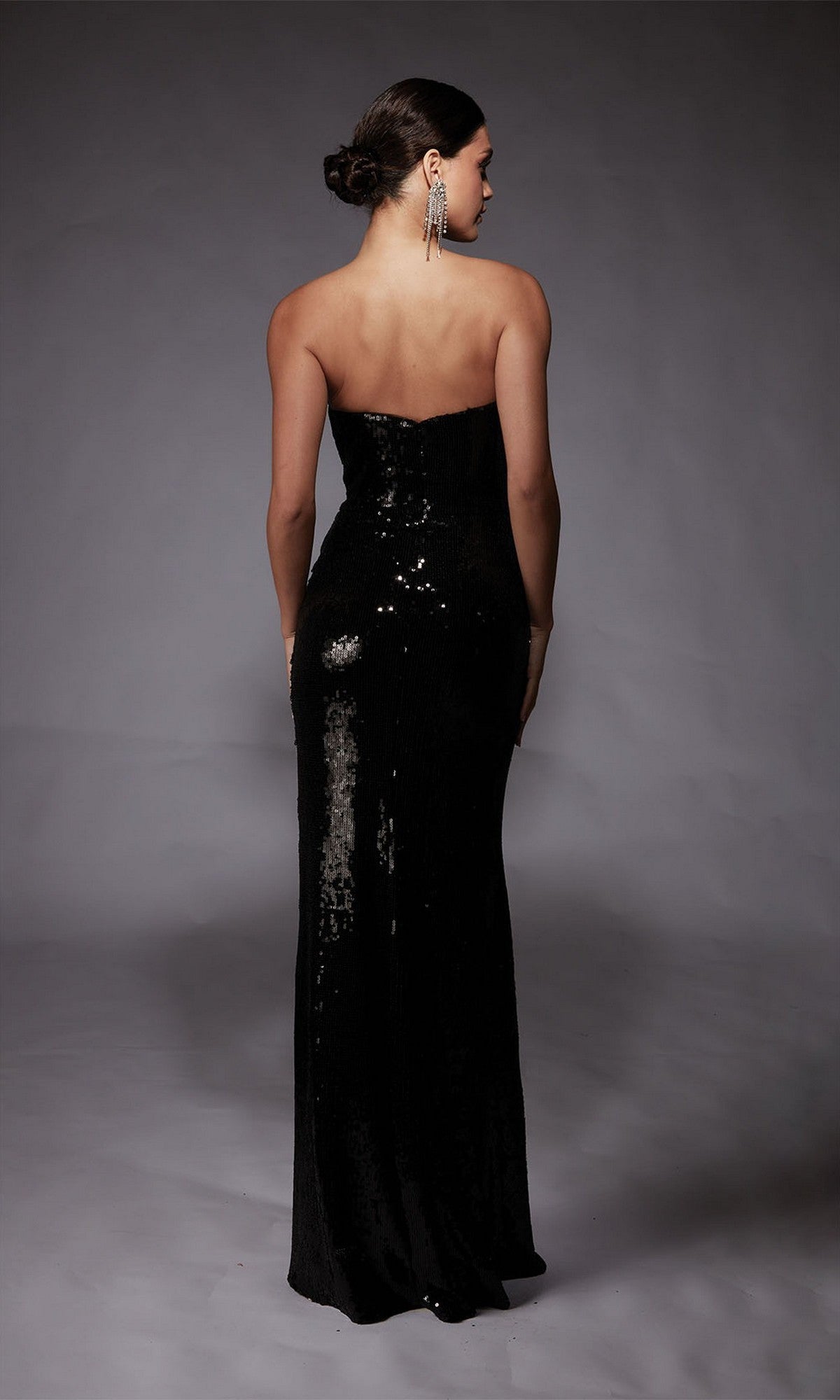 A woman wearing the Alyce 27704 long formal strapless dress, embellished with black sequins, stands with her back to the camera against a gray backdrop.