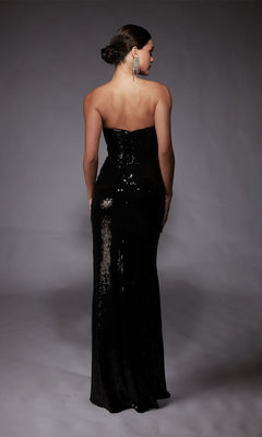 A woman wearing the Alyce 27704 long formal strapless dress, embellished with black sequins, stands with her back to the camera against a gray backdrop.