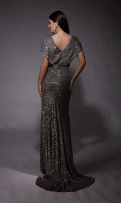 A woman models the Alyce 27708 long formal dress in silver sequins with cap sleeves, a draped back, and beaded waistband, standing against a neutral backdrop.