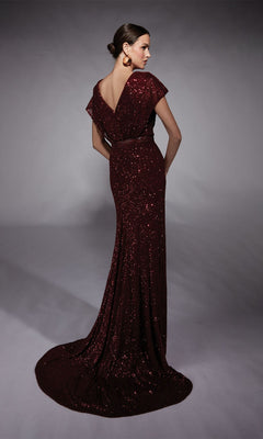 A woman stands on a grey backdrop wearing the Alyce 27708 long formal dress, a dark red sequin evening gown featuring a deep V-back, cap sleeves, and a beaded waistband. Her hair is styled in a low bun.