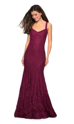 A woman stands, smiling with flowing hair, wearing the La Femme 27709 Open-Back Lace Mermaid Prom Dress—sleeveless, fitted, floor-length, and burgundy.