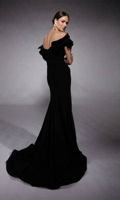 A woman stands against a plain gray backdrop, looking over her shoulder in the Alyce 27714 long formal dress—an elegant off-shoulder black gown with a sheath silhouette and sweeping train.
